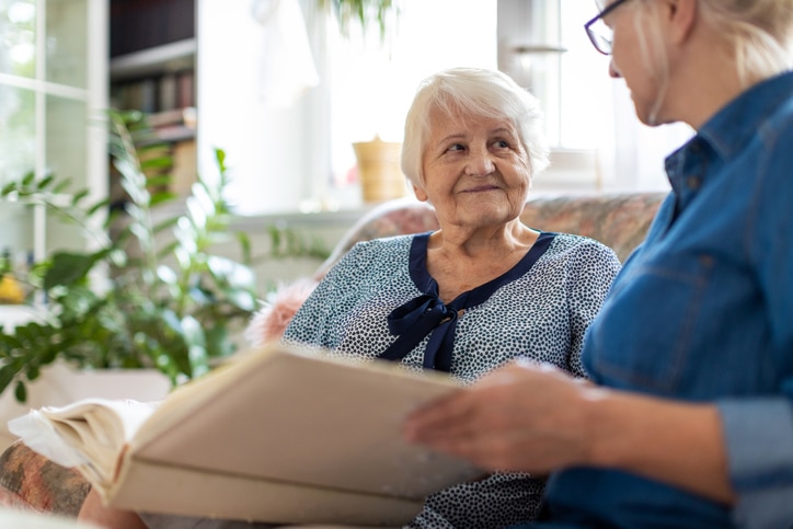 Senior woman and her adult daughter looking at photo album together on couch in living room